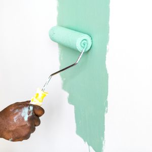 A hand rolls mint green paint onto a white wall, leaving a smooth stripe.