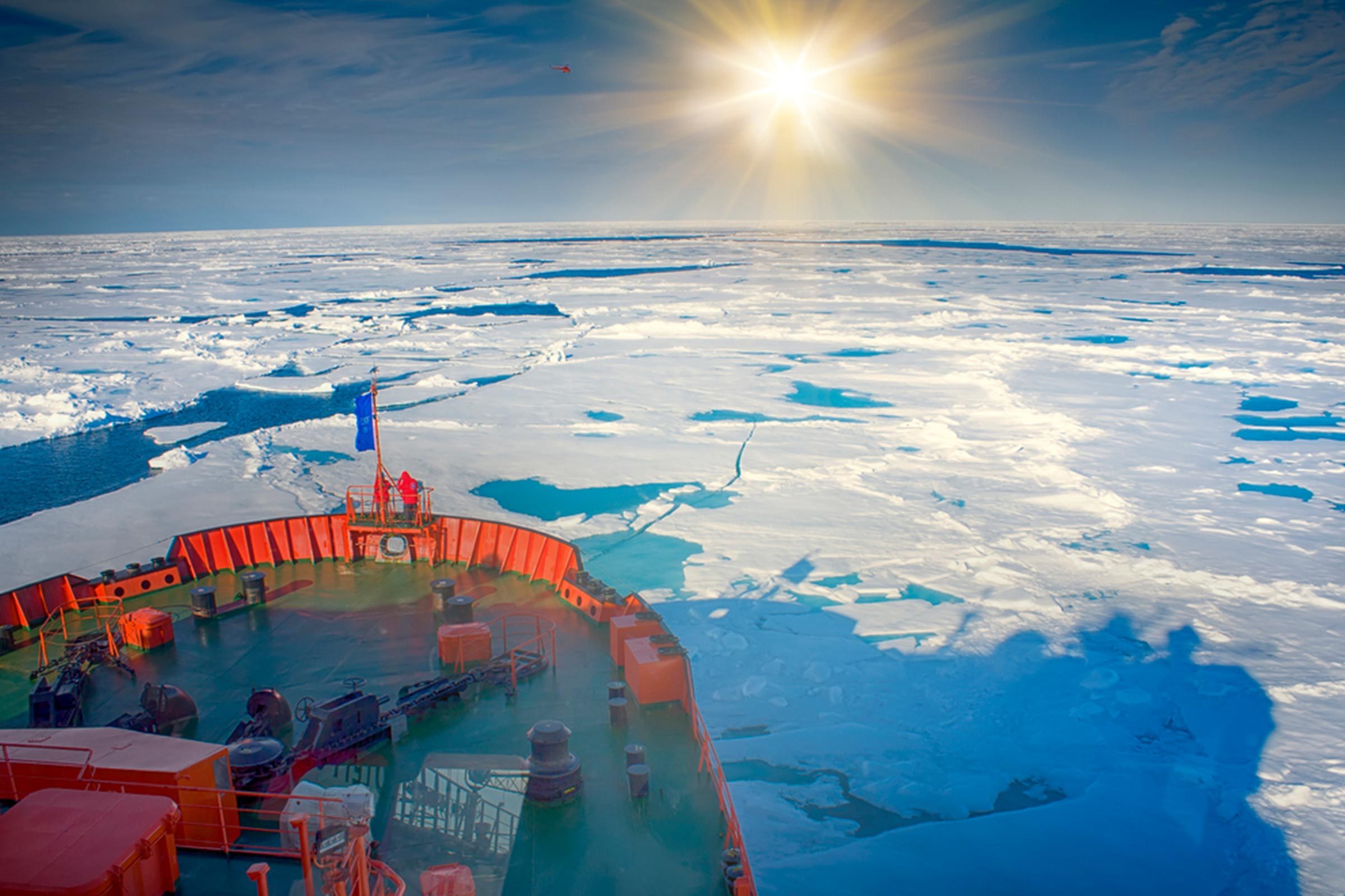 Ship navigates through icy waters under bright sun, surrounded by vast, frozen landscape.