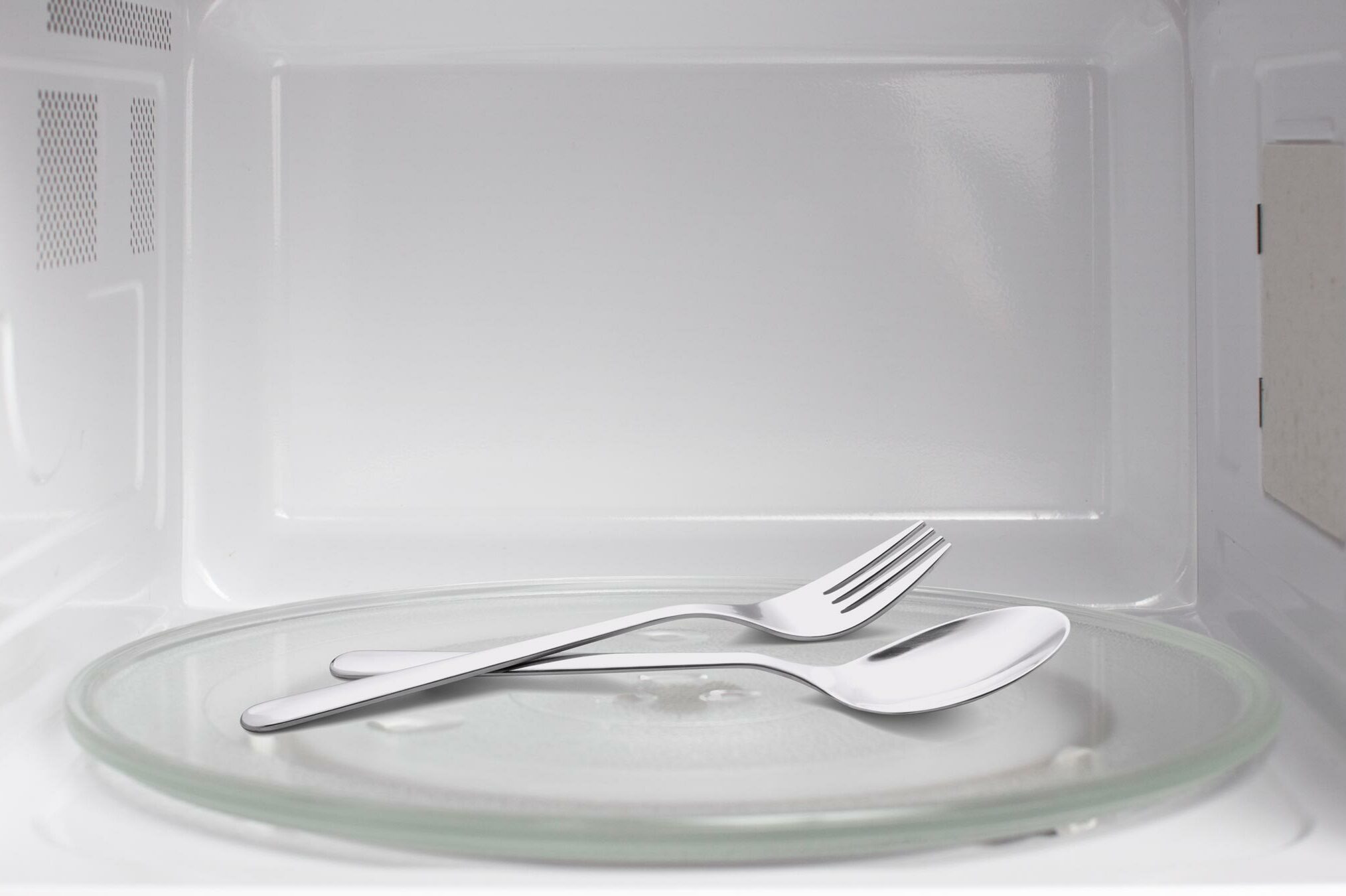 Fork and spoon resting inside a microwave with a clean, reflective interior.