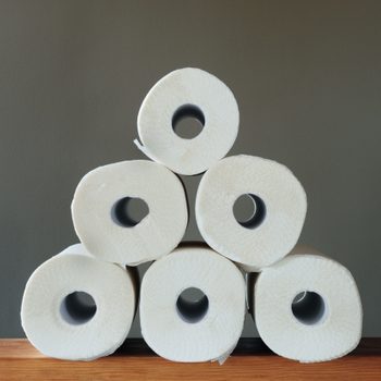 Rolls of toilet paper stacked in a pyramid shape on a wooden surface against a plain background.