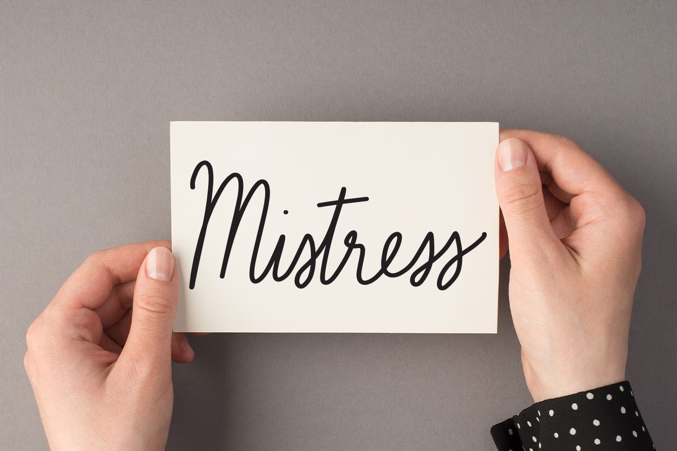 Hands hold a card reading "Mistress" in elegant script against a smooth, gray background.