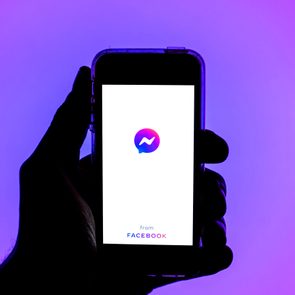 Hand holds smartphone displaying Messenger logo, reading 