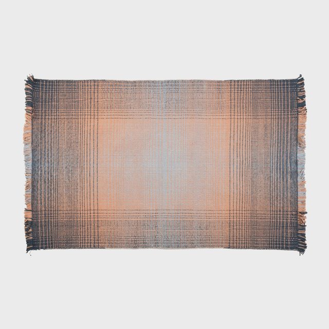 Woven rug displays intricate plaid pattern with fringed edges, lying flat on a plain background.