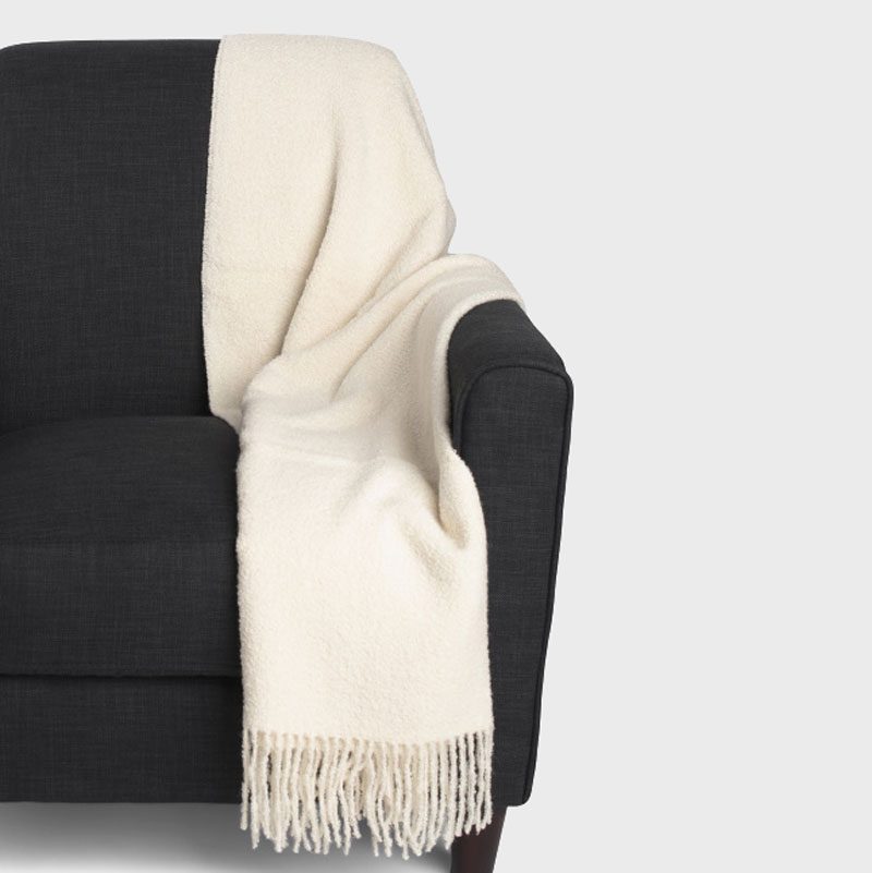 A cream-colored blanket drapes over a dark gray armchair, set against a plain white background.