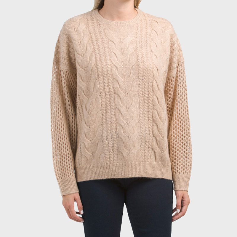 A beige cable-knit sweater, worn by a person standing, features intricate patterns on sleeves and front.
