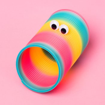 A colorful slinky with googly eyes lies on a pink background, creating a playful appearance.