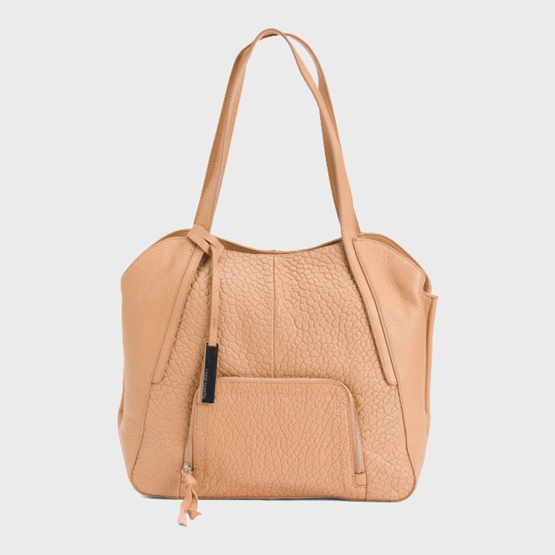 Tan textured handbag sits upright, featuring long handles and a front zippered pocket, against a plain gray background.