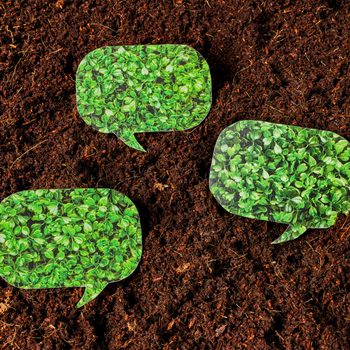 Green speech bubble cutouts rest stationary on dark, textured soil.