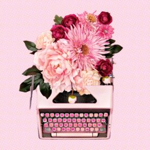 Typewriter holds blooming pink and white flowers, creating a vibrant floral arrangement, set against a soft pink background.