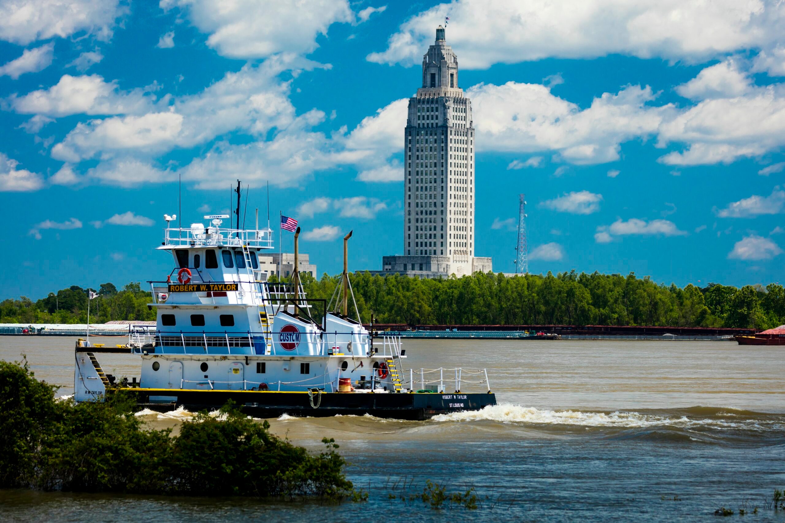 Barge floating on a wide river with a tall capitol building in the background