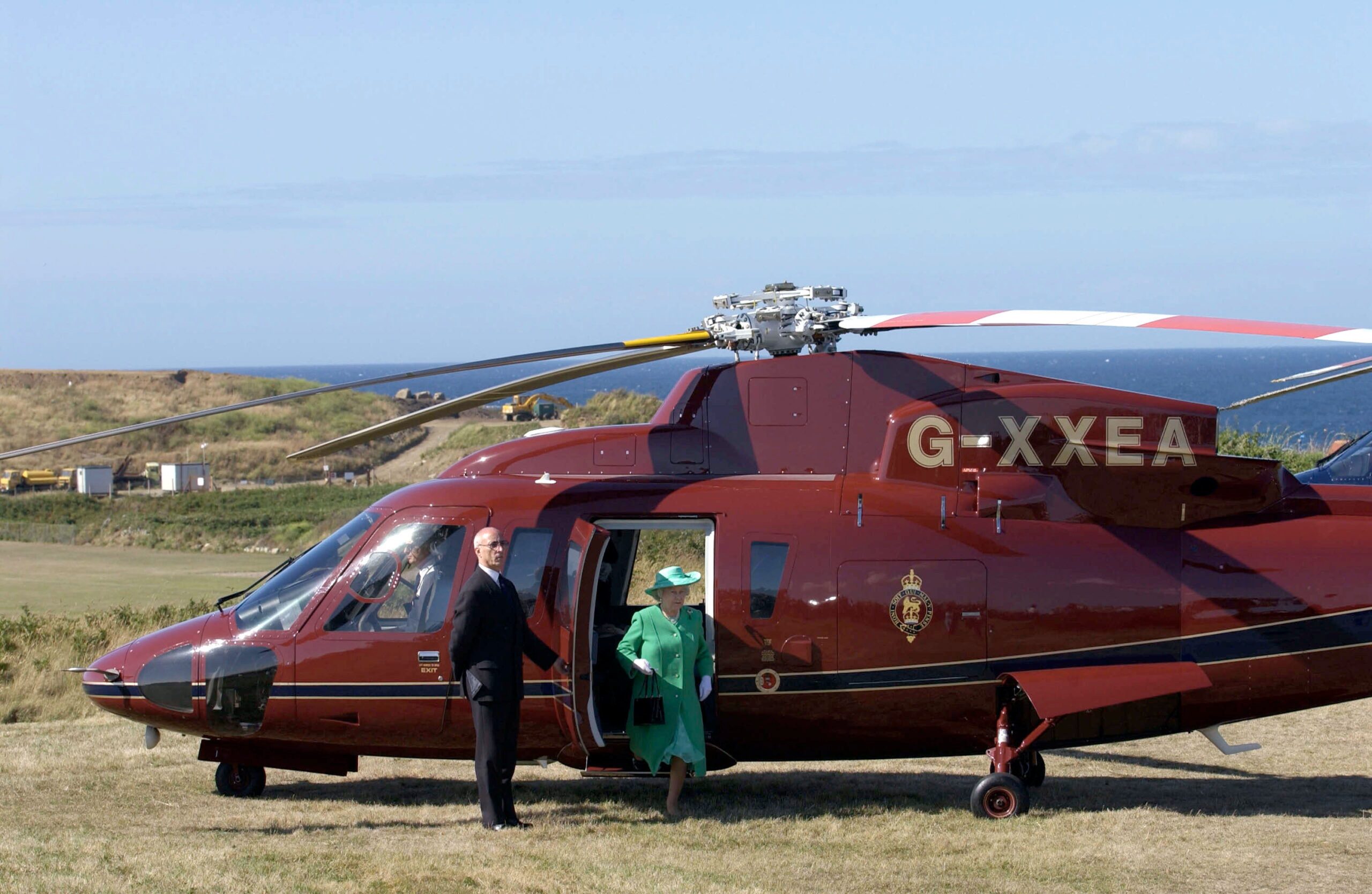 Queen Elizabeth steps out of a dark red helicopter on a barren landscape