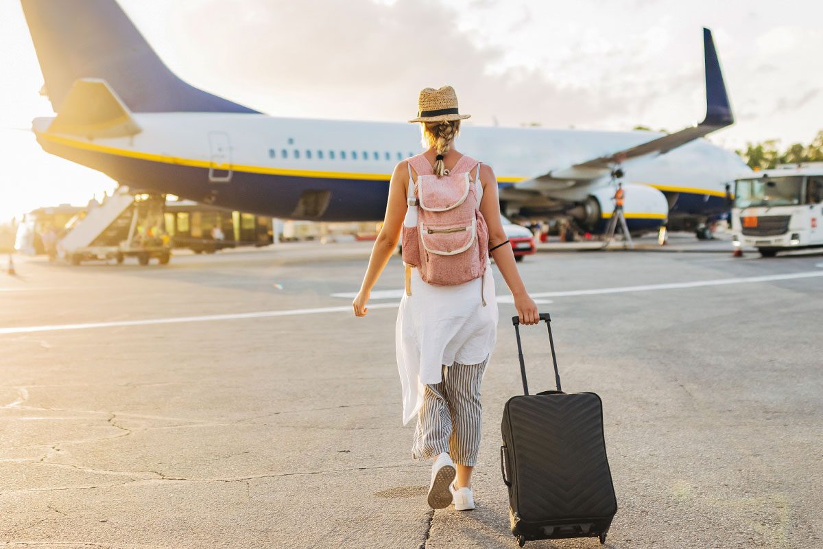 A female tourist walks towards the plane on the runway, dragging personal luggage behind her and carrying a backpack on her back