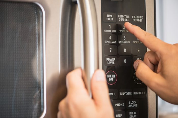 close up of hands pressing buttons on a microwave