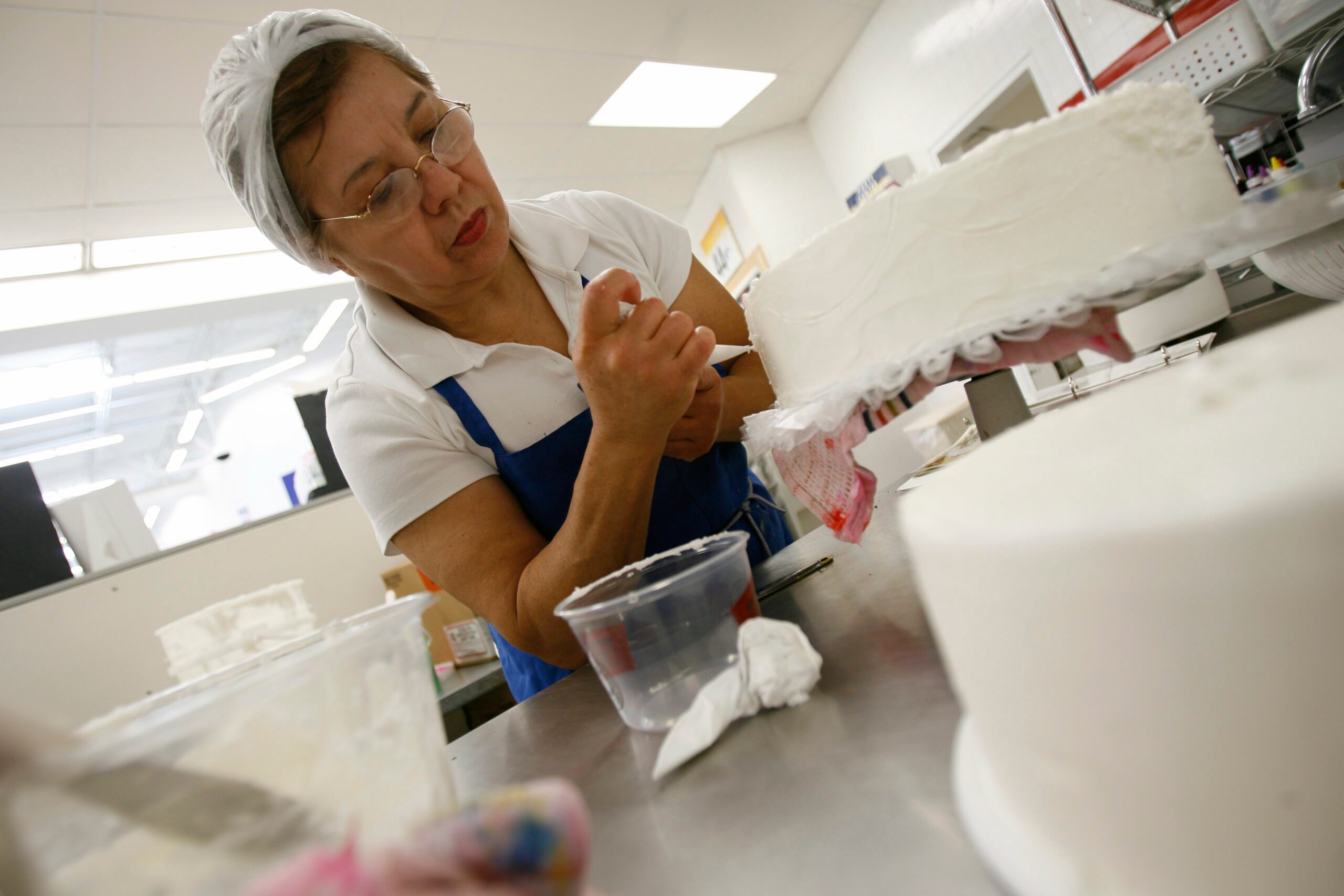 Woman decorates a white cake with icing at Walmart bakery
