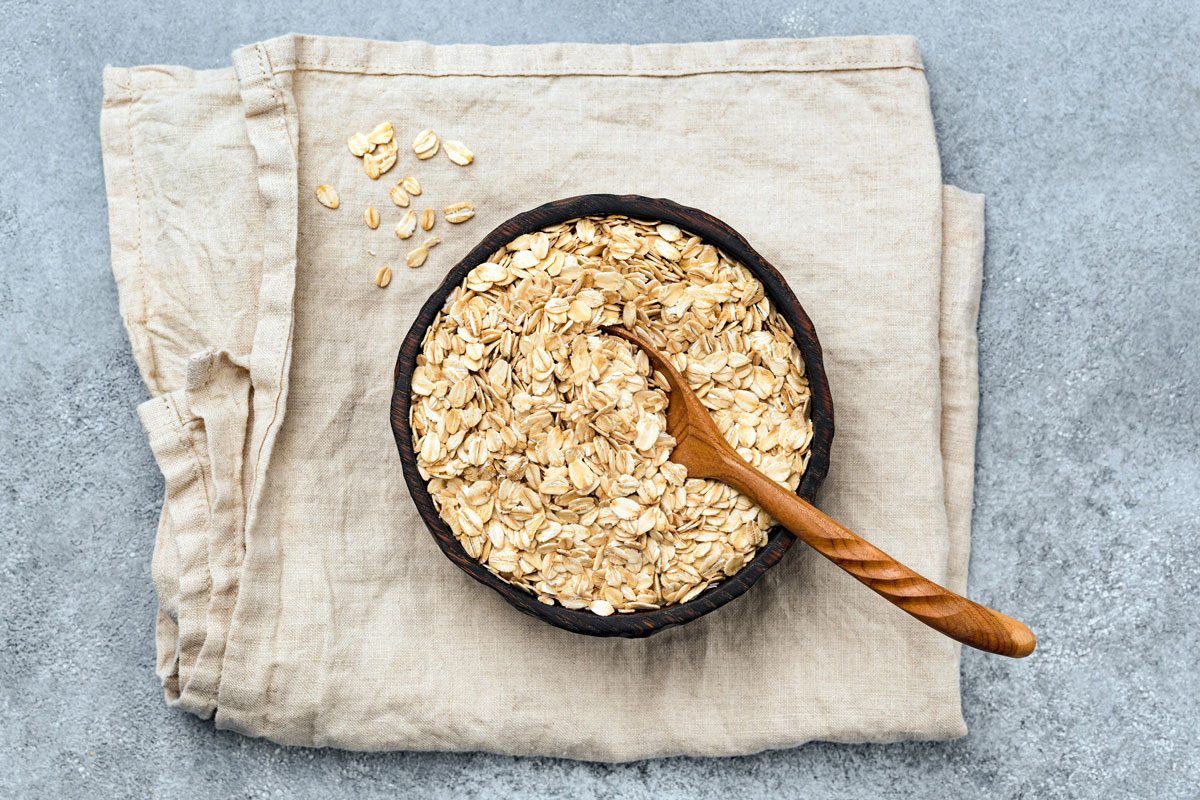 Rolled Oats Or Oat Flakes In Wooden Bowl On Linen Textile