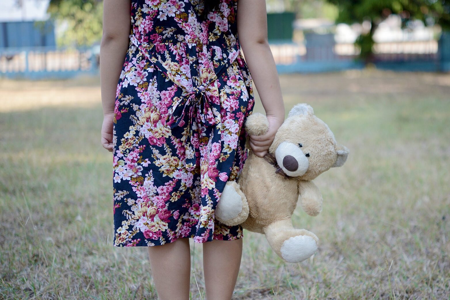 Little girl wearing pink flower dress dragging the teddy bear walking in the park, Domestic violence against children emotional concept