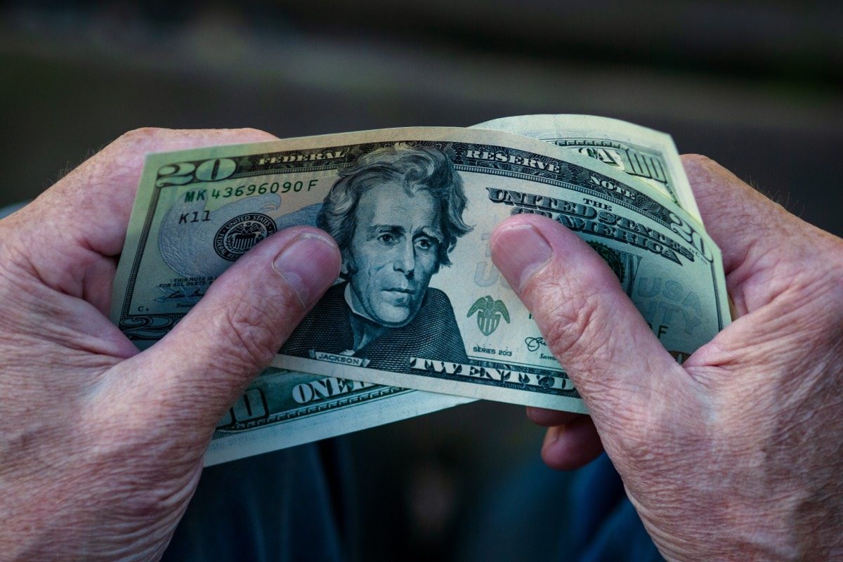 Elderly man holding US dollar bills in hands, 20 dollar note in pensioner's hand